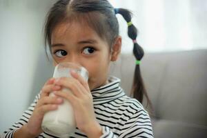 Asian little cute kid holding a cup of milk in the house. feel happy and enjoy drinking milk. photo