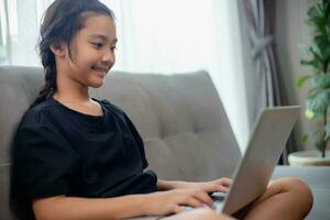 contento niña aprendizaje el Inglés idioma en línea con un ordenador portátil a hogar. foto