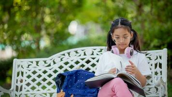 espalda a escuela. asiático niña leyendo un libro. primario colegio estudiantes después clases aprendizaje tarea. foto