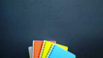 a stack of colorful notebooks on a blackboard video
