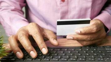 uma homem segurando uma crédito cartão e digitando em uma teclado video