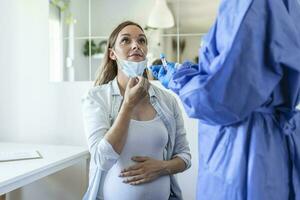 Healthcare worker with protective equipment performs coronavirus swab on pregnant woman.Nose swab for Covid-19. photo