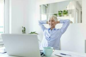 Focused old woman with white hair at home using laptop. Senior stylish entrepreneur working on computer at home. Woman analyzing and managing domestic bills and home finance photo