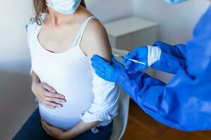 embarazada vacunación. médico dando codicioso -19 coronavirus vacuna inyección a embarazada mujer. médico vistiendo azul guantes vacunar joven embarazada mujer en clínica. personas vacunación concepto. foto