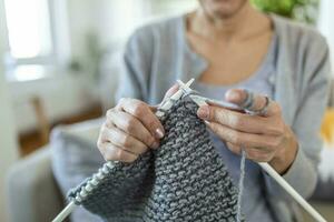 Close up view grandmother hands holding needles make repetitive motion knitting sitting on couch creating something with her arms. Hand knitting improve brain function, older generation hobby concept photo