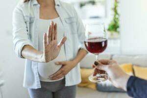 Pregnant woman refusing a glass of wine. Alcohol In Pregnancy. Unrecognizable Expectant Lady Gestring Stop To Offered Glass Of Wine photo
