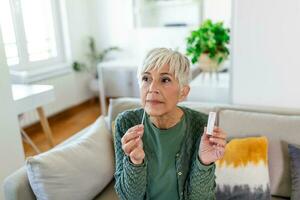 Mature woman taking a Self-swabbing home tests for COVID-19 at home with Antigen kit. Introducing nasal stick to check the infection of Coronavirus. Quarantine, pandemic. photo