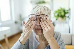 Mature woman holds glasses with diopter lenses,rubs her eyes and looks through them, the problem of myopia, vision correction photo