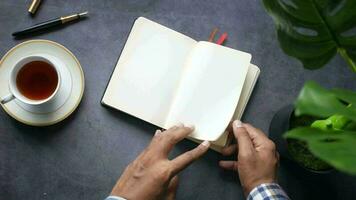 a man's hands writing in a notebook with a cup of coffee on a table video