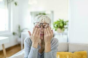 Mature woman holds glasses with diopter lenses,rubs her eyes and looks through them, the problem of myopia, vision correction photo