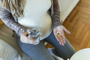 Cropped view of sick and ill pregnant woman holding different pills on palm hand, showing medical preparat on camera photo