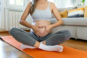 Closeup shot of an unrecognizable pregnant woman making a heart shape with her hands on her belly at home photo