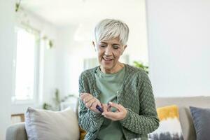 Mature Woman using lancelet on finger. woman doing blood sugar test at home in a living room. photo