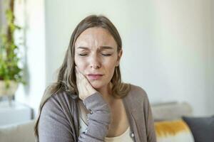 diente dolor y odontología. joven mujer sufrimiento desde terrible fuerte dientes dolor, conmovedor mejilla con mano. hembra sensación doloroso dolor de muelas. dental cuidado y salud concepto. foto