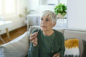 Mature woman taking a Self-swabbing home tests for COVID-19 at home with Antigen kit. Introducing nasal stick to check the infection of Coronavirus. Quarantine, pandemic. photo