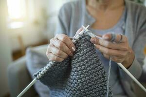 Close up view grandmother hands holding needles make repetitive motion knitting sitting on couch creating something with her arms. Hand knitting improve brain function, older generation hobby concept photo