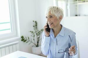 mayor mujer utilizando su teléfono. contento mujer relajante a hogar, ella es hablando en su teléfono inteligente foto