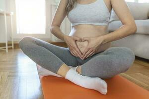 Closeup shot of an unrecognizable pregnant woman making a heart shape with her hands on her belly at home photo