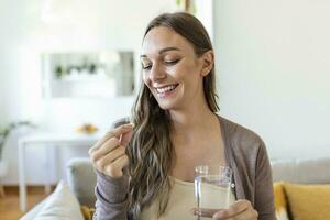 cabeza Disparo retrato contento mujer sostiene píldora vaso de agua, toma diario medicina vitamina d, omega 3 suplementos, piel pelo uña fortalecer y belleza, medicación para salud cuidado concepto foto