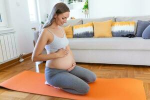 pregnant woman training yoga in hero pose, caressing her belly. Young happy expectant relaxing, thinking about her baby and enjoying her future life. Motherhood, pregnancy, yoga concept photo