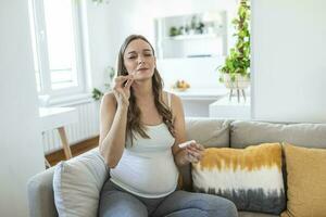 Pregnant woman sitting at a living room of a house with people, introducing a nasal swab in the nose to take an antigen coronavirus test, a Covid-19 rapid PCR to check sars infection. photo