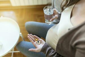 Cropped view of sick and ill pregnant woman holding different pills on palm hand, showing medical preparat on camera photo