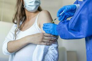 Female doctor giving Covid-19 vaccine injection to young pregnant woman at health centre. Expectant lady being immunized against coronavirus at clinic. Population vaccination concept photo