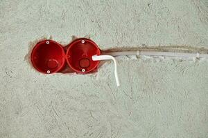 Plastic socket box and electrical wires on plastered wall photo