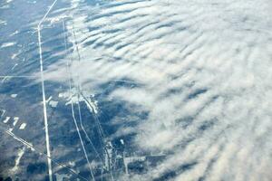 Aerial view from airplane window over clouds top to snow covered rivers, fields and roads photo
