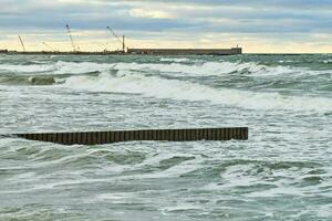 View of blue sea with foaming waves and wooden breakwaters photo