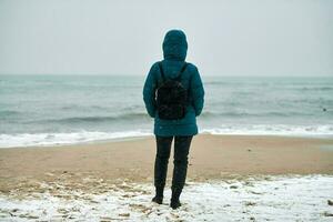 Girl in down jacket standing on seashore in winter photo