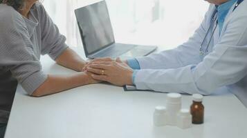 Doctor giving hope. Close up shot of young female physician leaning forward to smiling elderly lady patient holding her hand in palms. Woman caretaker in white coat supporting encouraging old person photo