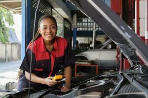 uno negro hembra profesional automotor mecánico trabajador cheques un ev coche batería y híbrido motor a un mantenimiento cochera, experto eléctrico vehículo servicio, y fijación ocupaciones auto industria. foto