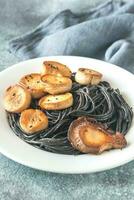 Portion of black pasta with king oyster scallops photo