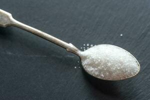 Spoon with white sugar on the dark background photo