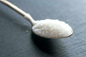 Spoon with white sugar on the dark background photo