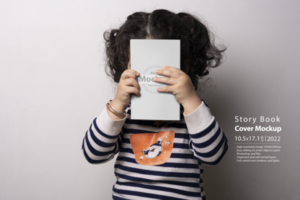 pequeno menina segurando uma crianças história livro com em branco cobrir dentro frente do dela face psd