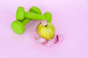 un verde manzana, y un centímetro medición cinta en un rosado antecedentes. Deportes, Deportes nutrición, sano comiendo, dieta. espacio para el texto. foto