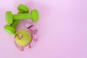 un verde manzana, y un centímetro medición cinta en un rosado antecedentes. Deportes, Deportes nutrición, sano comiendo, dieta. espacio para el texto. foto