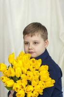 retrato de un joven, hermosa chico. sostiene un enorme brazada de Fresco amarillo tulipanes el concepto de primavera y día festivo, marzo 8, internacional De las mujeres día foto