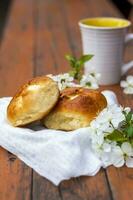 Baked open rolls and a cup of coffee on a dark, worn rustic wooden table. The composition is decorated with a twig with white flowers. Cherry tree flowers. Selective focus. photo