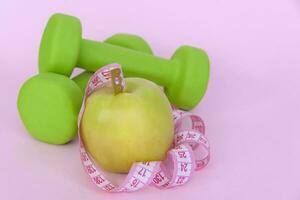 A green apple, and a centimeter measuring tape on a pink background. Sports, sports nutrition, healthy eating, diet. Space for the text. photo