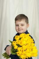 retrato de un joven, hermosa chico. sostiene un enorme brazada de Fresco amarillo tulipanes el concepto de primavera y día festivo, marzo 8, internacional De las mujeres día foto