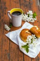Baked open rolls and a cup of coffee on a dark, worn rustic wooden table. The composition is decorated with a twig with white flowers. Cherry tree flowers. Selective focus. photo