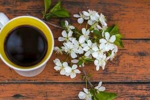 una taza de café sobre una mesa de madera rústica oscura y gastada. la composición está decorada con una ramita con flores blancas. flores de cerezo. enfoque selectivo. foto
