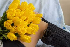 A bouquet of fresh yellow tulips lies on the lap of a young girl. The legs of a girl in knitted knee socks. Spring flowers as a gift. The concept of spring and holiday, March 8, International photo