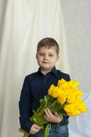 Portrait of a young, beautiful boy. Holds a huge armful of fresh yellow tulips. The concept of spring and holiday, March 8, International Women's Day photo