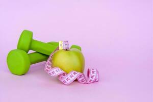 A green apple, and a centimeter measuring tape on a pink background. Sports, sports nutrition, healthy eating, diet. Space for the text. photo