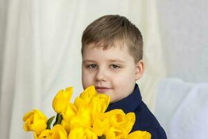 retrato de un joven, hermosa chico. sostiene un enorme brazada de Fresco amarillo tulipanes el concepto de primavera y día festivo, marzo 8, internacional De las mujeres día foto