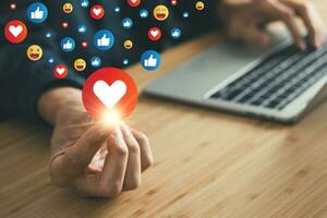 man holding heart emoji social media icon, thumbs up and smiling faces with laptop background. social network concept. photo